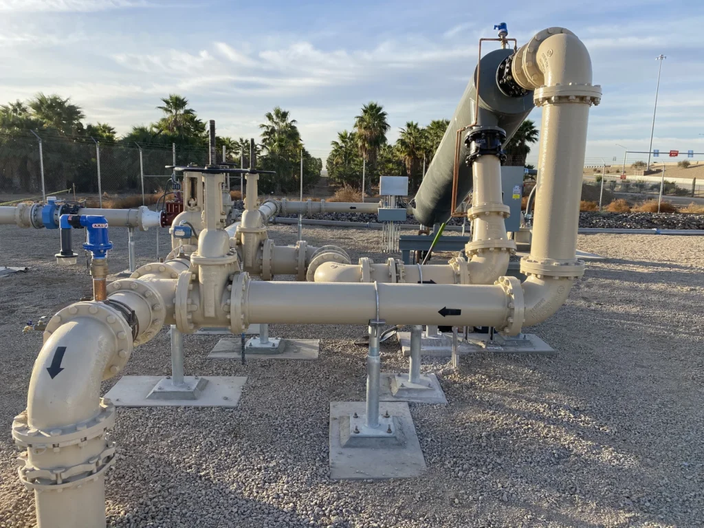 Water well pump station piping and valves with palm trees in the background