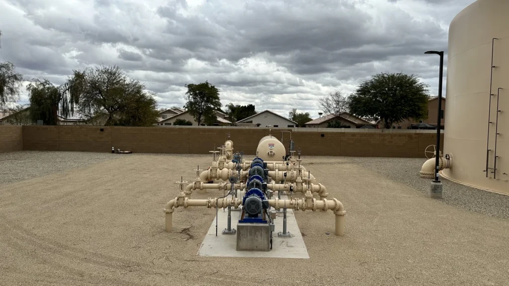 Pump station valve manifold and piping on a concrete pad adjacent to a water storage tank