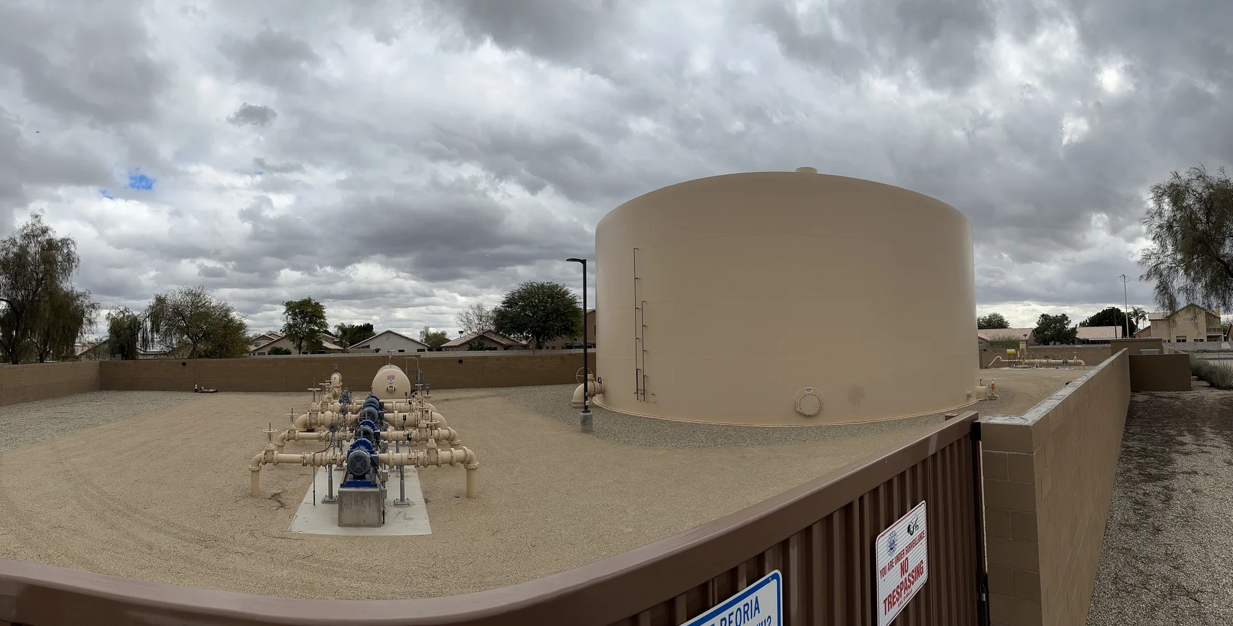 Panoramic view of a water storage tank and valve manifold from behind a perimeter wall
