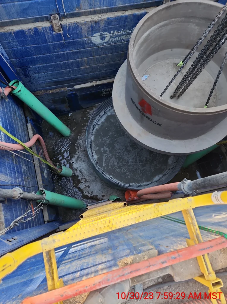 Overhead view of a concrete manhole installation with utility pipes in a shored trench