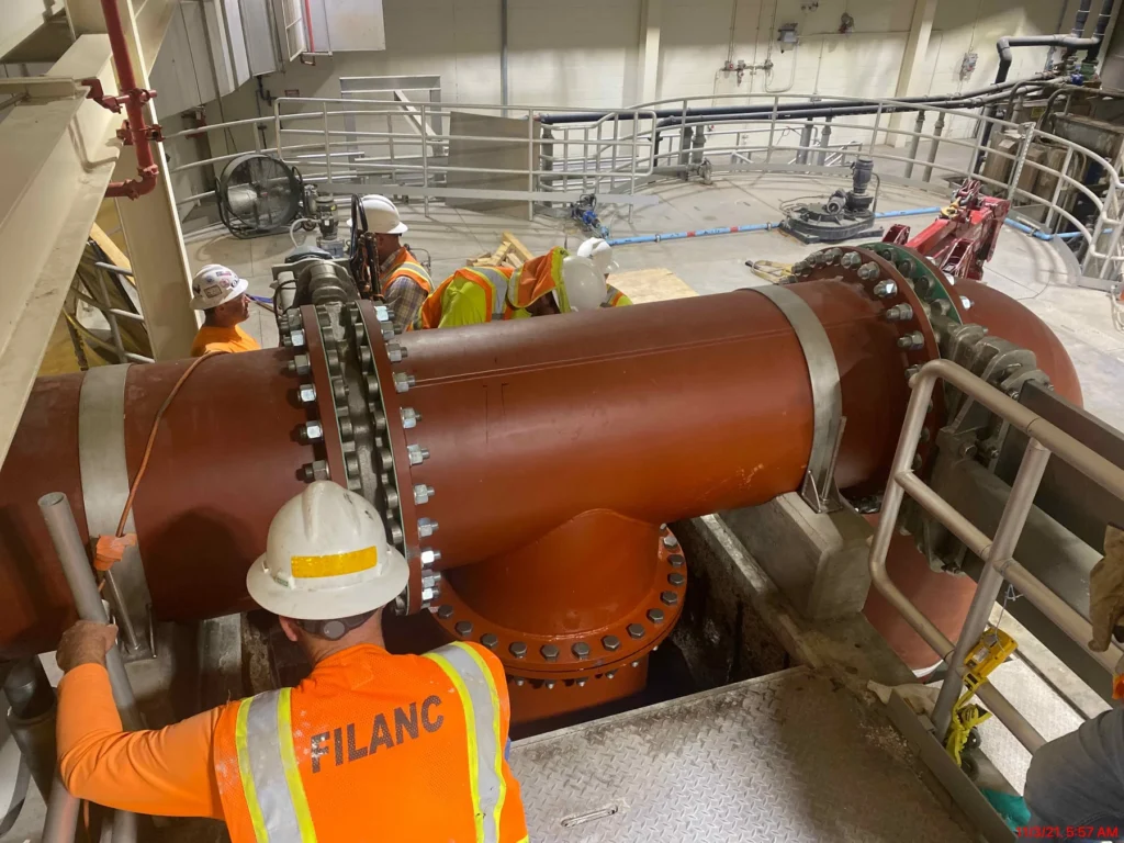 Construction crew inspecting a large-diameter flanged water main inside a pump station facility