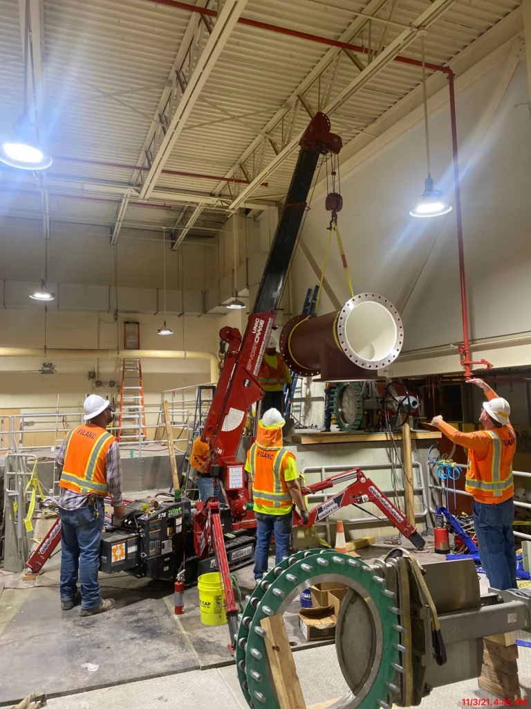 Crew using a mini crane to lift a large pipe section inside a water treatment pump station