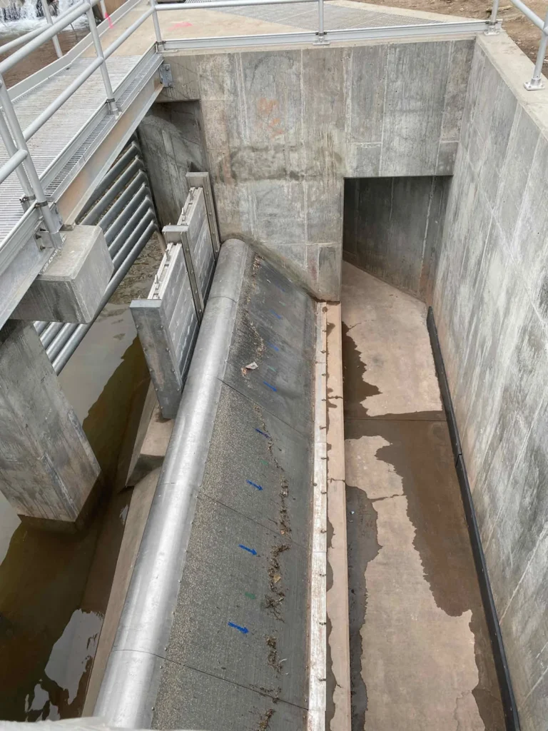 Deep concrete channel structure with large-diameter pipe and metal railings at pump station