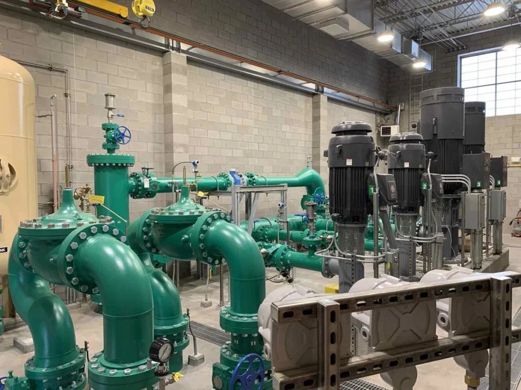 Interior pump room showing green piping network, valves, and vertical turbine pumps