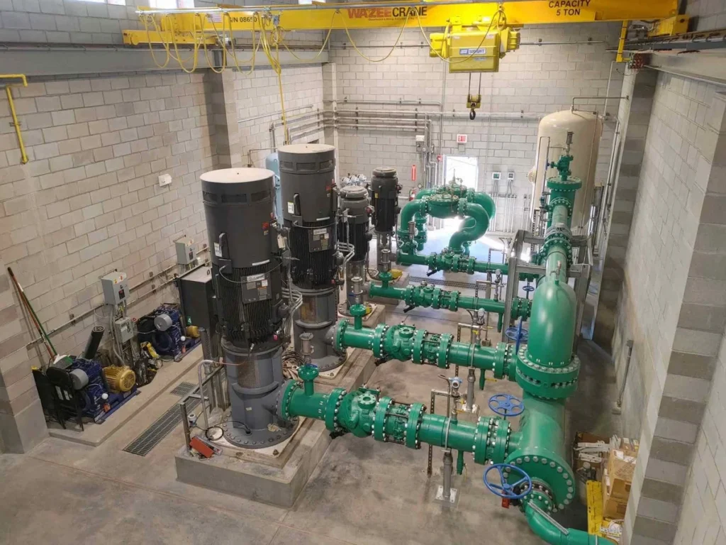 Overhead view of pump room interior with green piping, vertical pumps, and overhead crane system