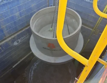 Concrete manhole structure being lowered by crane into a shored trench