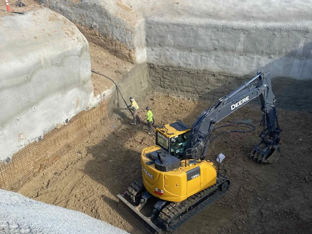 Excavator performing deep excavation work with shotcrete-stabilized walls for lift station construction