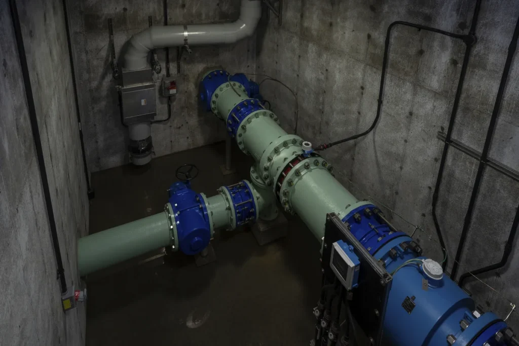 Underground valve room with green and blue flanged piping, check valves, and flow meter
