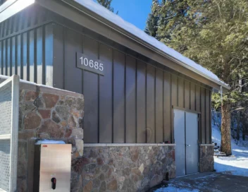 Completed booster pump station building with stone and metal siding in a snowy mountain setting