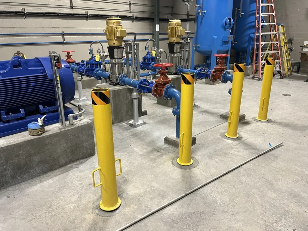 Interior of pump station with blue piping, yellow safety bollards, and motorized valve actuators