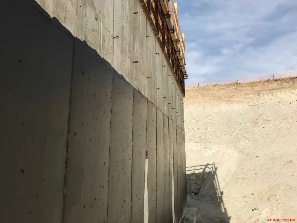 Tall concrete retaining wall with form tie holes and timber formwork at well house construction site