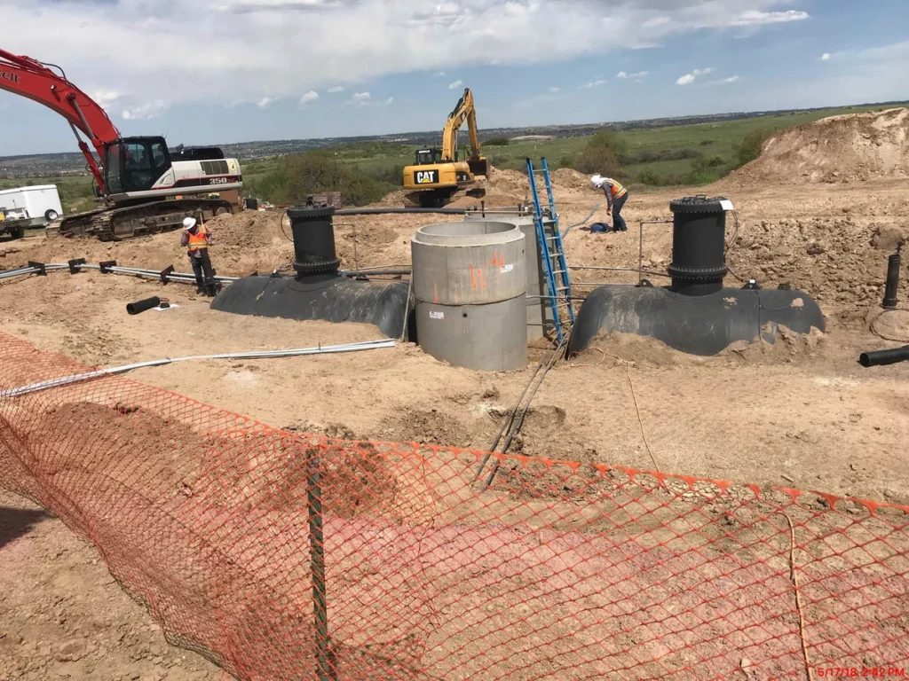 Workers installing precast concrete manholes with excavators at pipeline construction site