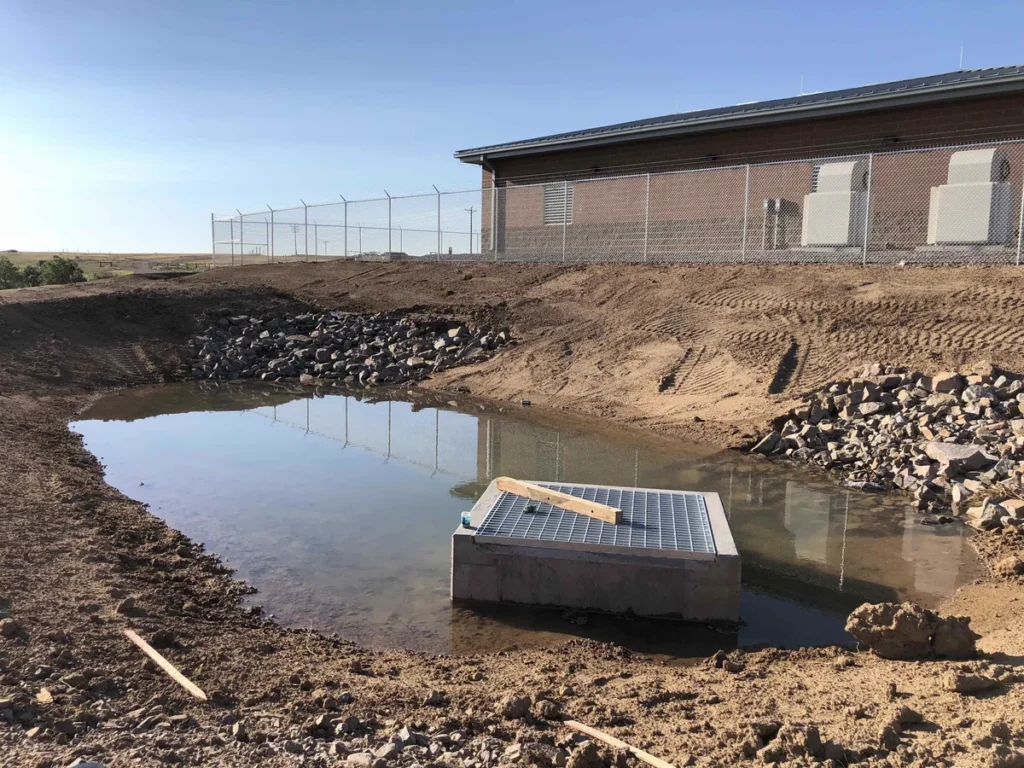 Stormwater detention basin with concrete inlet structure adjacent to well house building