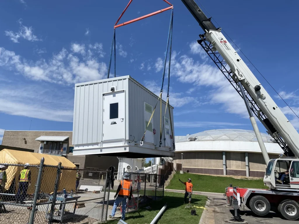 Crane lifting a prefabricated electrical building into position at water treatment facility