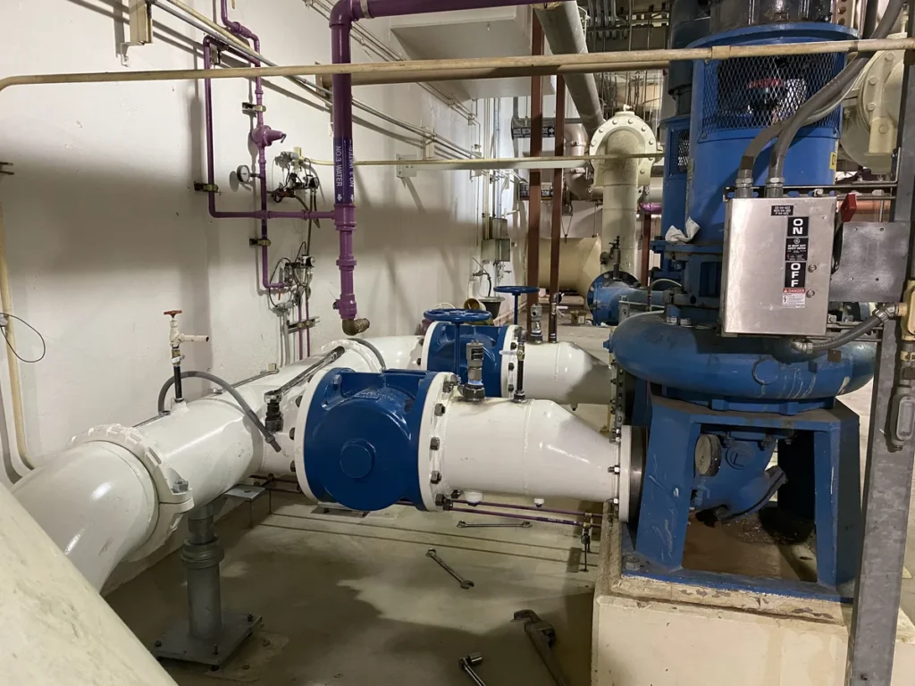 Existing pump room with white and blue piping, valves, and vertical pump motors