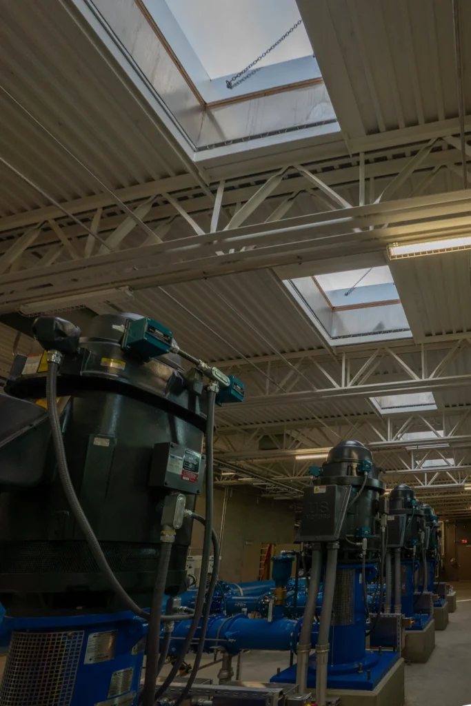 Pump room interior looking up through skylights with row of blue pumps and piping below