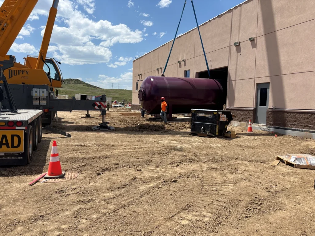 Crane unloading large purple surge tank from flatbed truck at WISE Pump Station construction site
